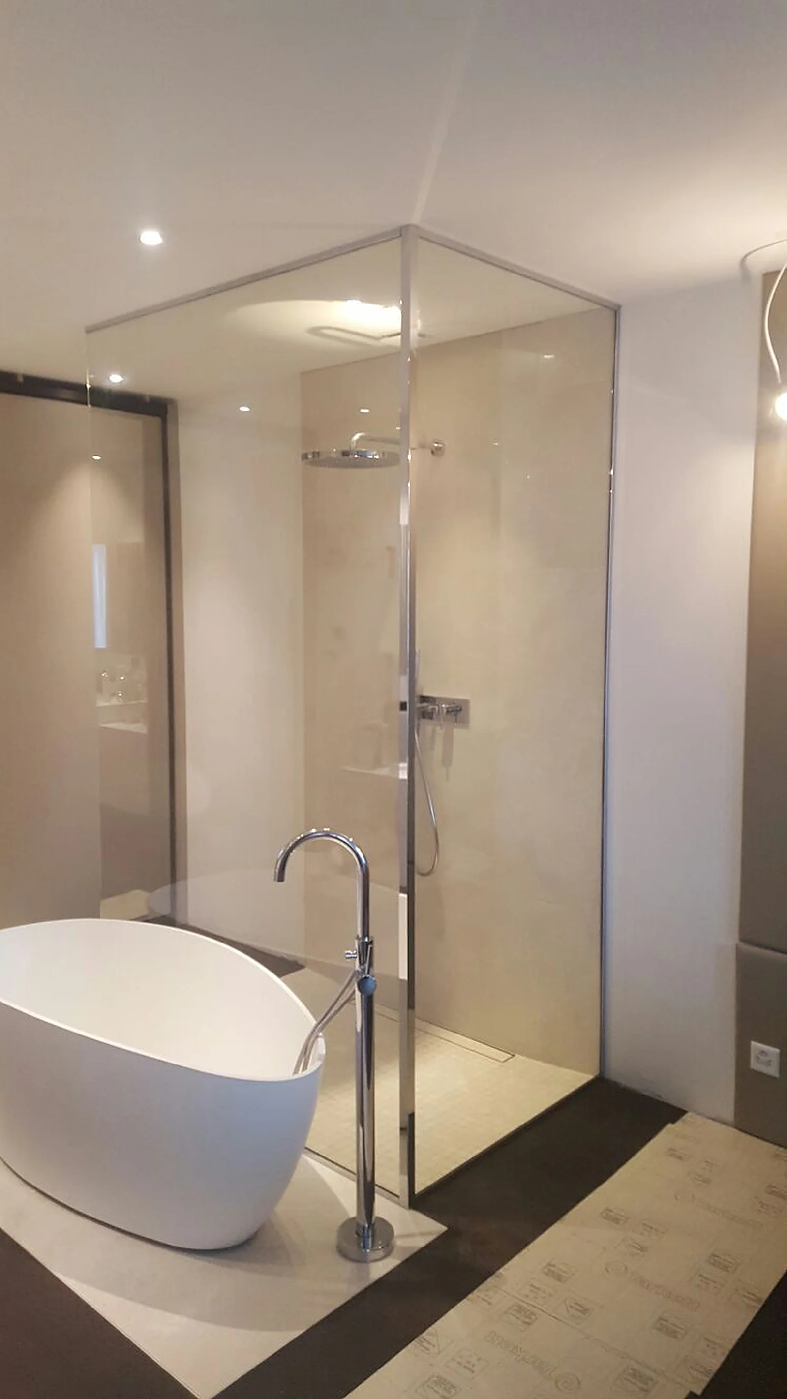 Paroi de douche d'angle en verre clair, à côté d'une baignoire îlot blanche